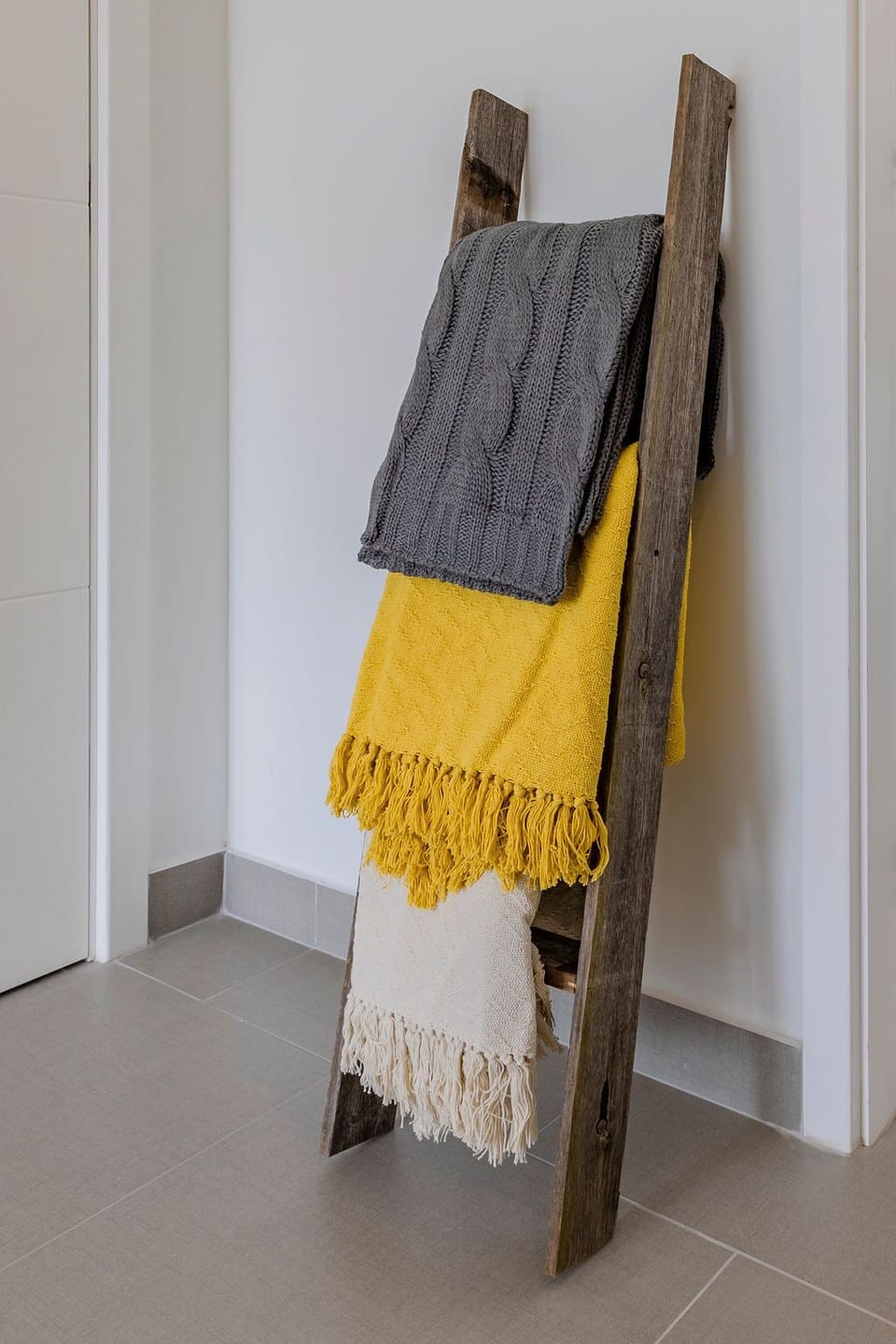 Cozy textured throws in warm yellows and grays await you on a rustic ladder, adding charm and comfort to your space.