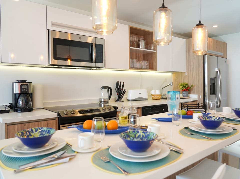 Gather around your bright, modern kitchen where warm pendant lights glow above a breakfast spread waiting just for you.