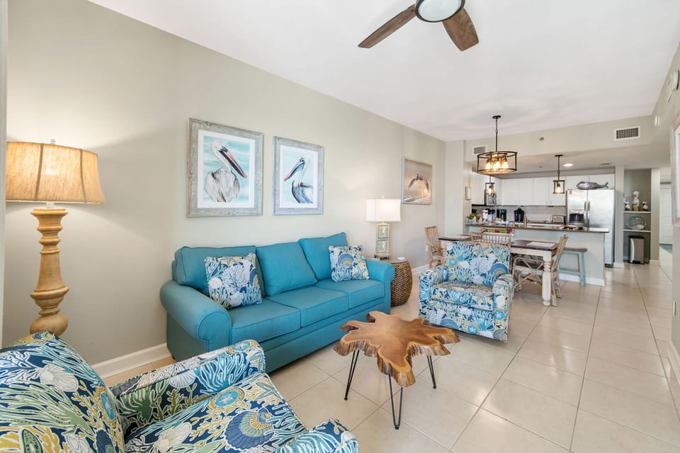 Relax in your coastal-inspired living space with turquoise seating and ocean artwork, flowing seamlessly into the modern kitchen.