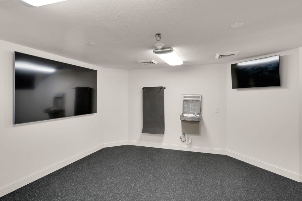 Your private workout space features wall-mounted screens, premium rubber flooring, and a convenient water station for staying hydrated during your fitness routine.