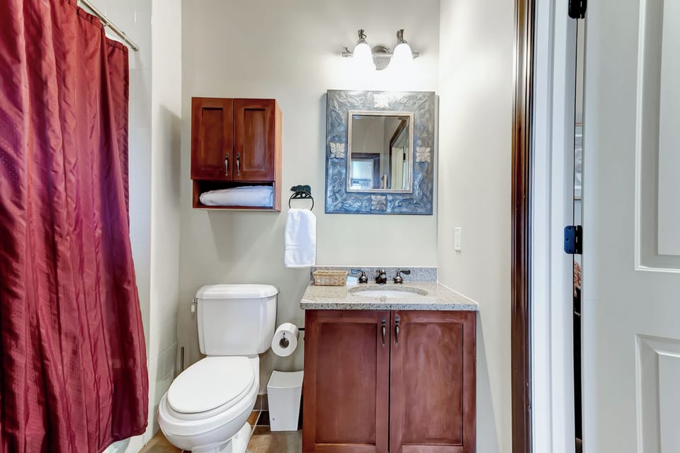- Compact bathroom with wood cabinetry and bright mirror lighting   - Includes full shower and modern amenities for guest use   - Conveniently located next to cozy twin bedroom