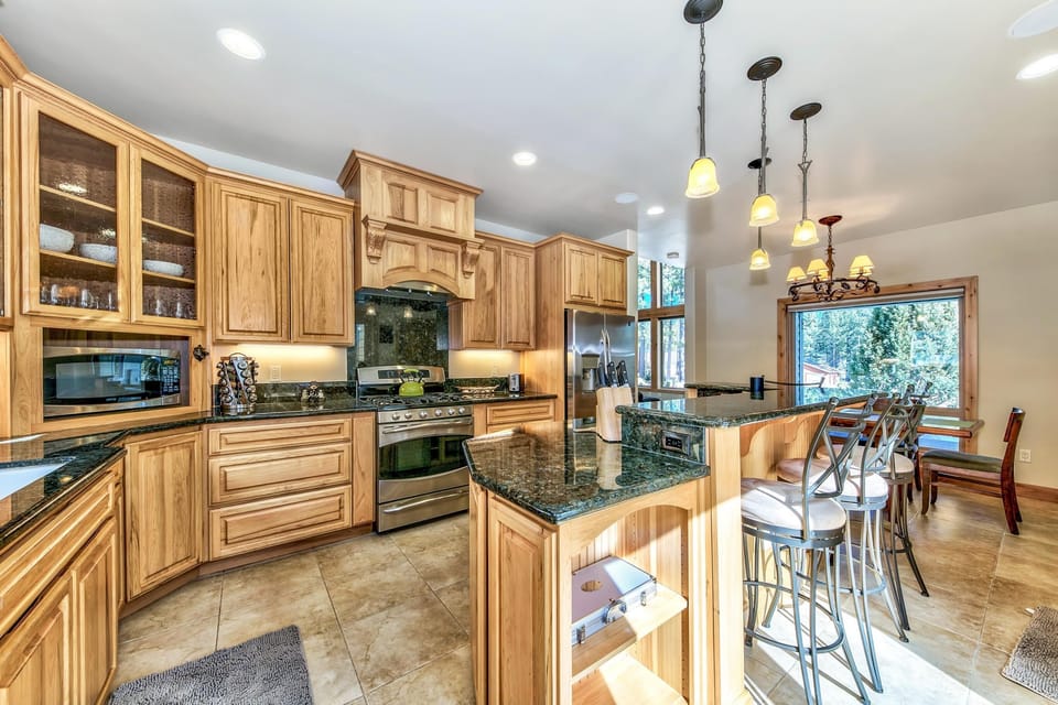Kitchen with natural wood cabinets, green granite countertops, stainless steel appliances, and a breakfast bar with metal stools.