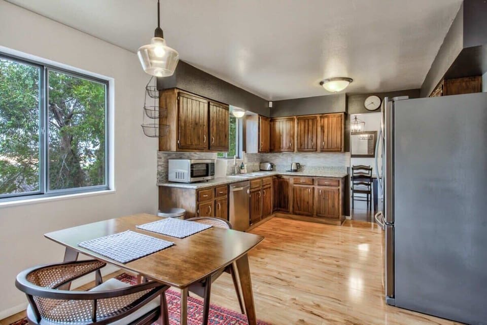 Bright kitchen with wood cabinets, stainless steel refrigerator, and a small dining table by the window. Natural light and an open layout make it easy to prep meals, pour a drink, and gather around the table.