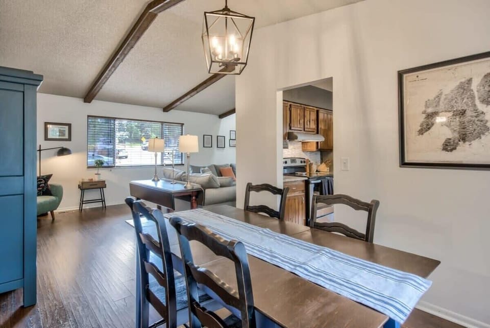 Dining area with a long wooden table and simple runner, framed by exposed ceiling beams and open views into the living space. A comfortable setting for shared meals, conversation, and slow mornings at the table.
