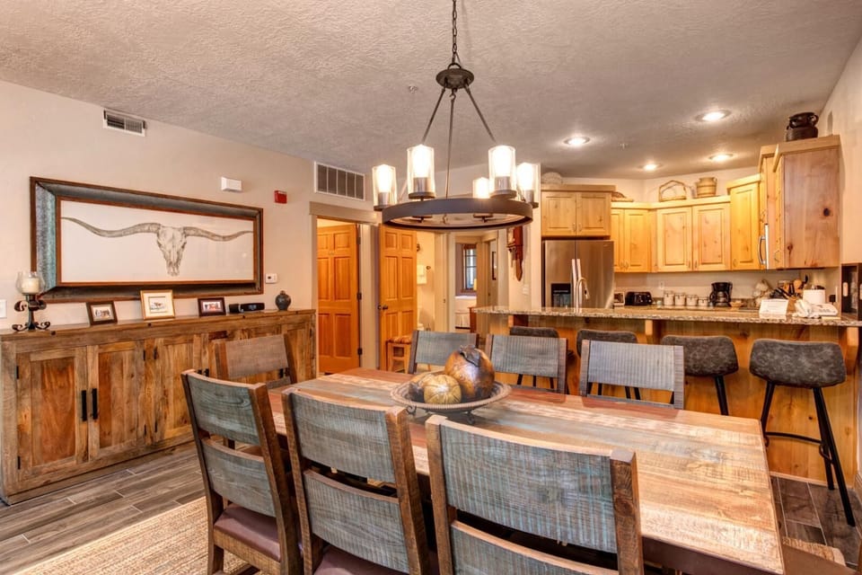 This spacious dining area features rustic charm, a central chandelier, and open sightlines to the kitchen and great room.