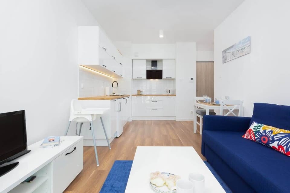 A living area with a vibrant blue sofa, a small dining table, and a large window.