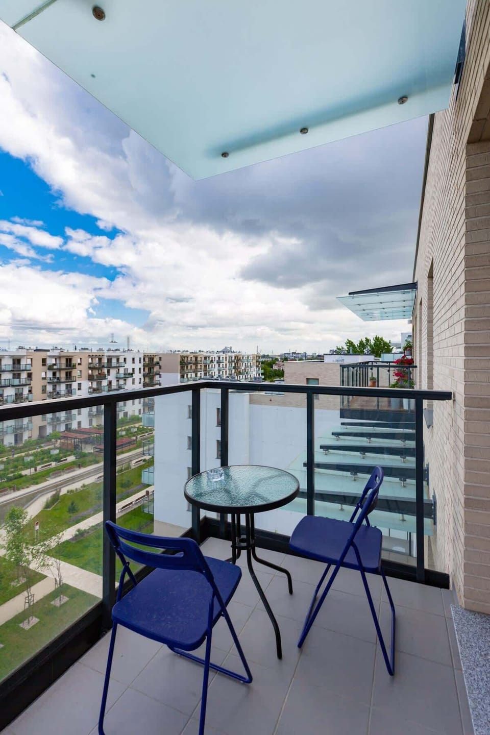 A small balcony with outdoor seating and a view of the nearby buildings and greenery.