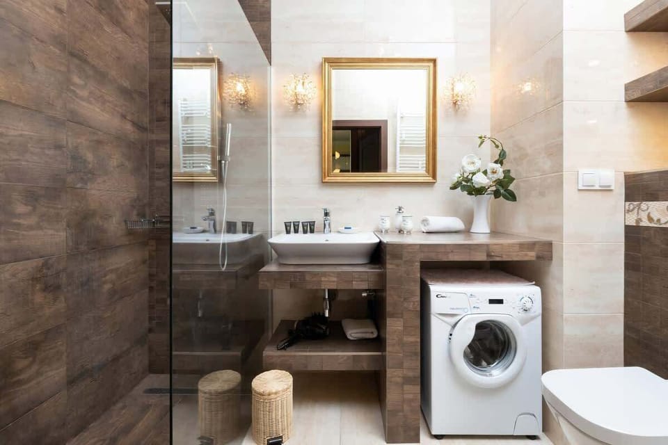 A modern bathroom featuring a washing machine, sink, and mirror with decorative lighting above.