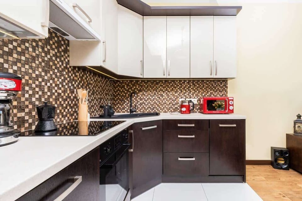 A compact kitchenette with white cabinets, a patterned backsplash, and red appliances, offering a stylish and functional space.
