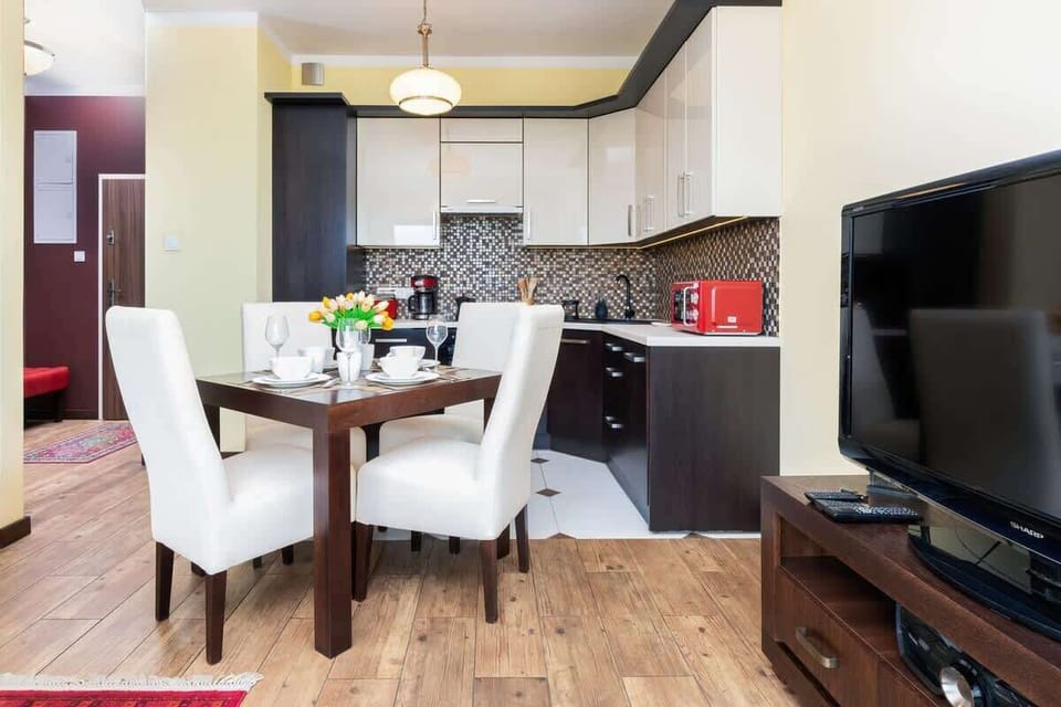 A modern kitchenette paired with a dining table for four, blending practicality and style, with sleek finishes and cozy lighting.