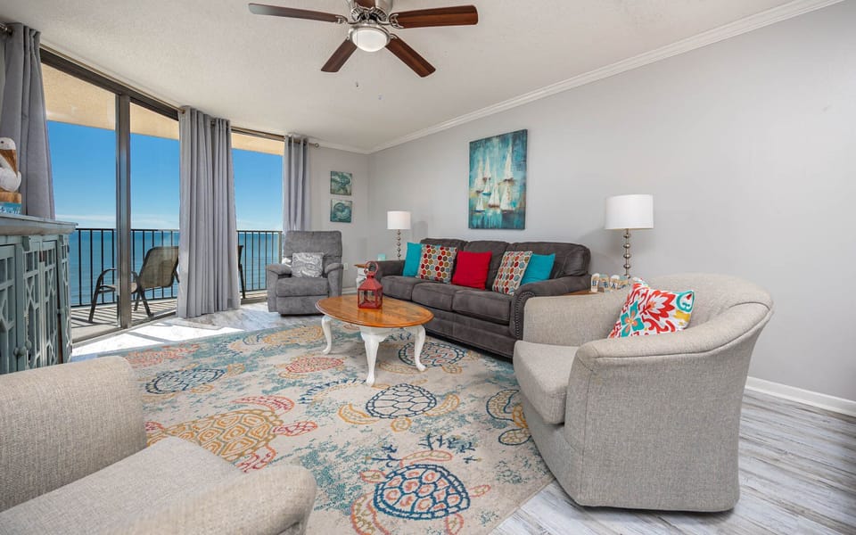 Bright living area featuring a gray sofa with queen sleeper and colorful pillows, a cozy rug, and views of the beach
