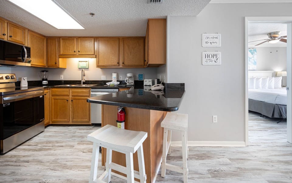 Bright kitchen features wooden cabinetry, a black countertop, and aspacious breakfast bar