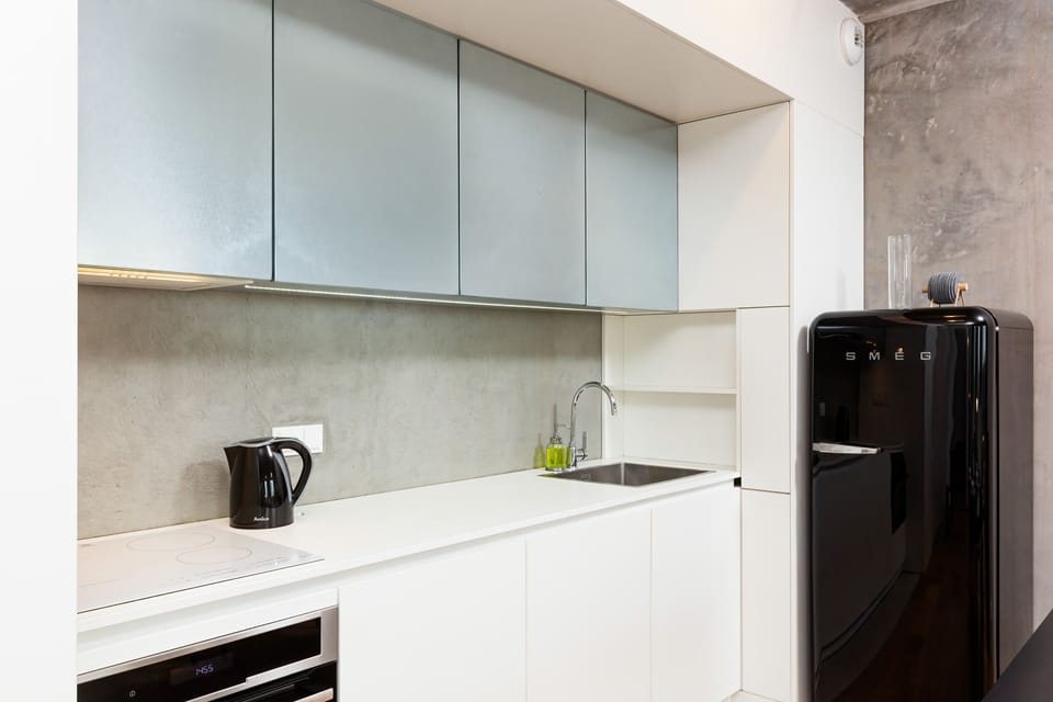A compact, modern kitchen with white cabinets, a black countertop, and essential appliances like a kettle and stove.