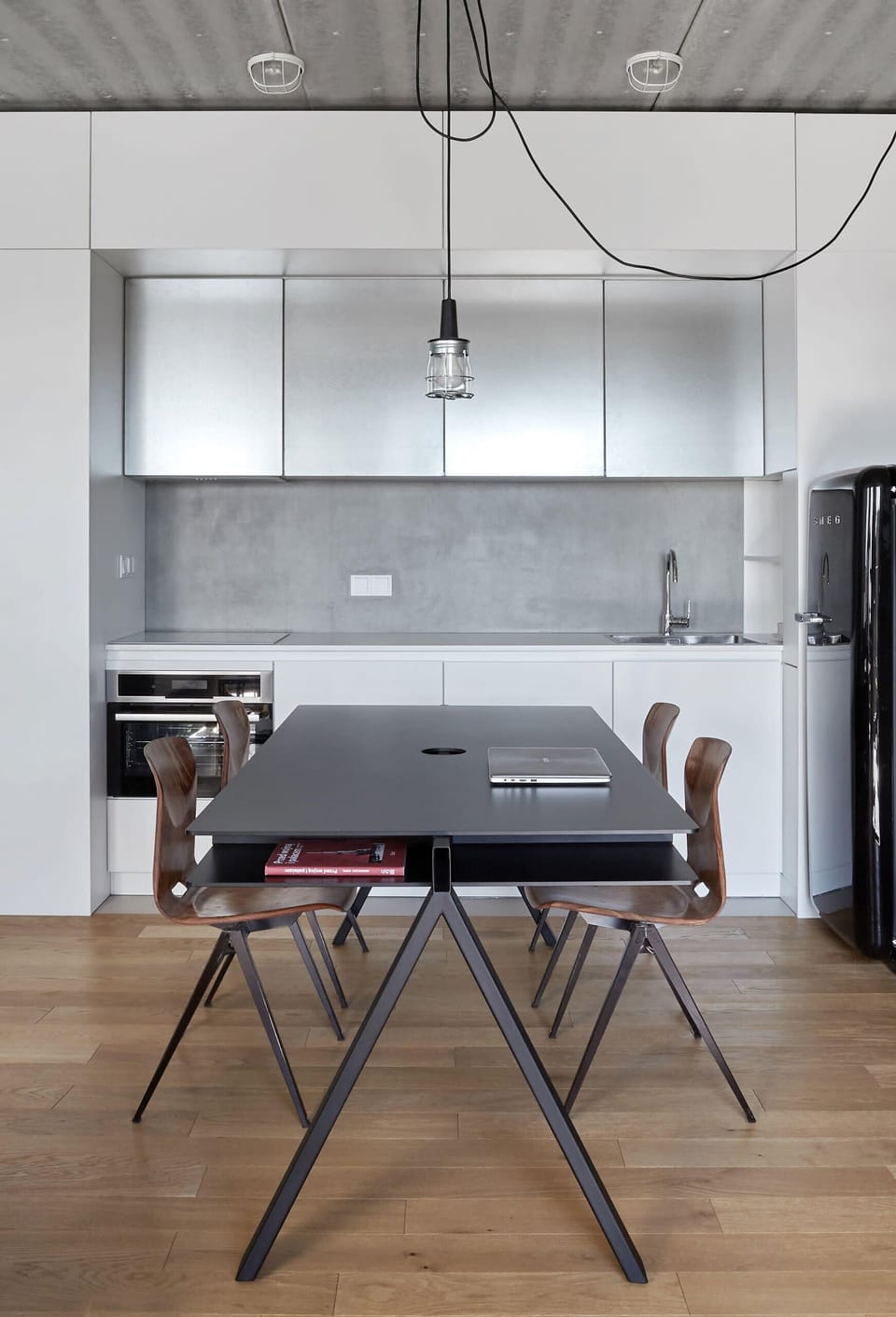 A modern dining table set for a meal, with sleek black chairs and a minimalist kitchenette in the background, featuring white cabinets and black countertops.