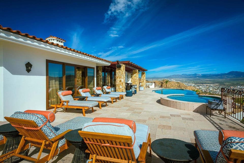 The pool deck at Casa Cielo at Pedregal, with sun loungers, an outdoor dining table and the infinity pool above Cabo San Lucas.