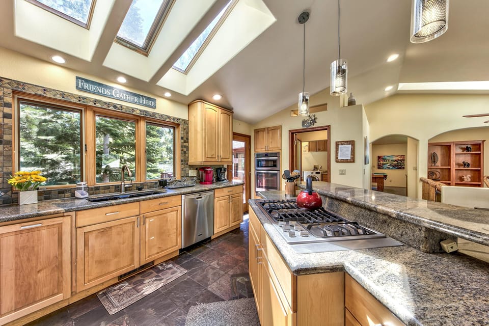 Kitchen with granite countertops, light wood cabinets, gas cooktop island, and skylights illuminating slate tile flooring.