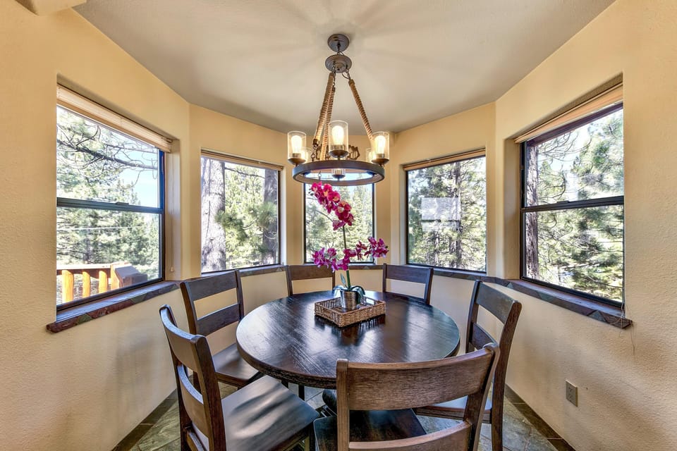 Five large windows surround the dining nook, offering forest views and natural light on slate tile flooring.