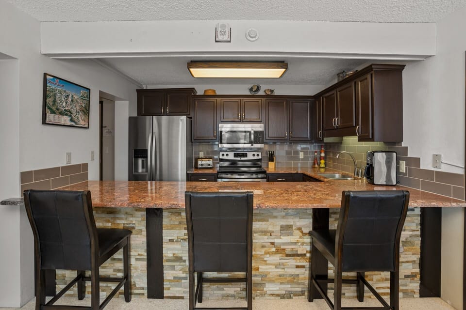 Stacked Stone base with Granite Countertop at Kitchen pass-through. Dark Brown Bar Stools for 3.