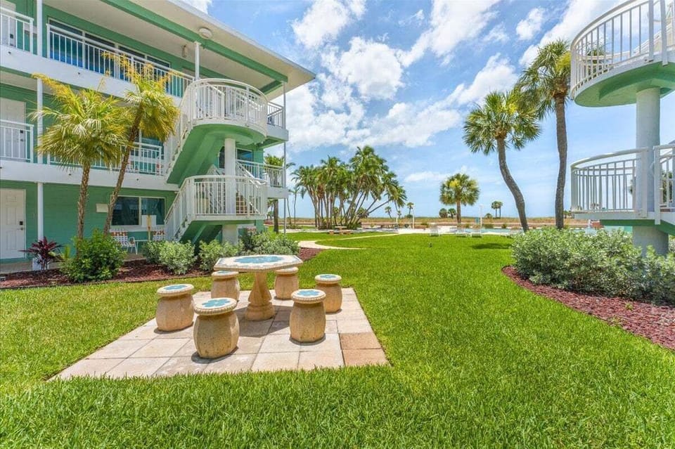 A beautifully landscaped tropical courtyard with stone patio seating, swaying palms, and stunning Gulf views