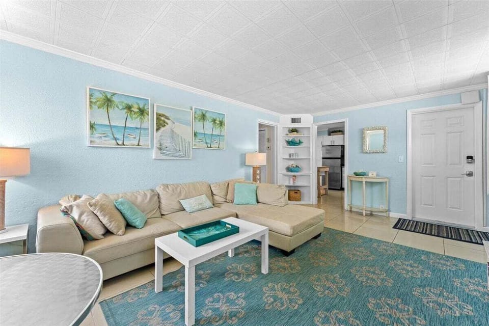 Bright living room with a smart TV, comfy sectional sofa, and a dining table for two — a relaxed coastal space to unwind after the beach.