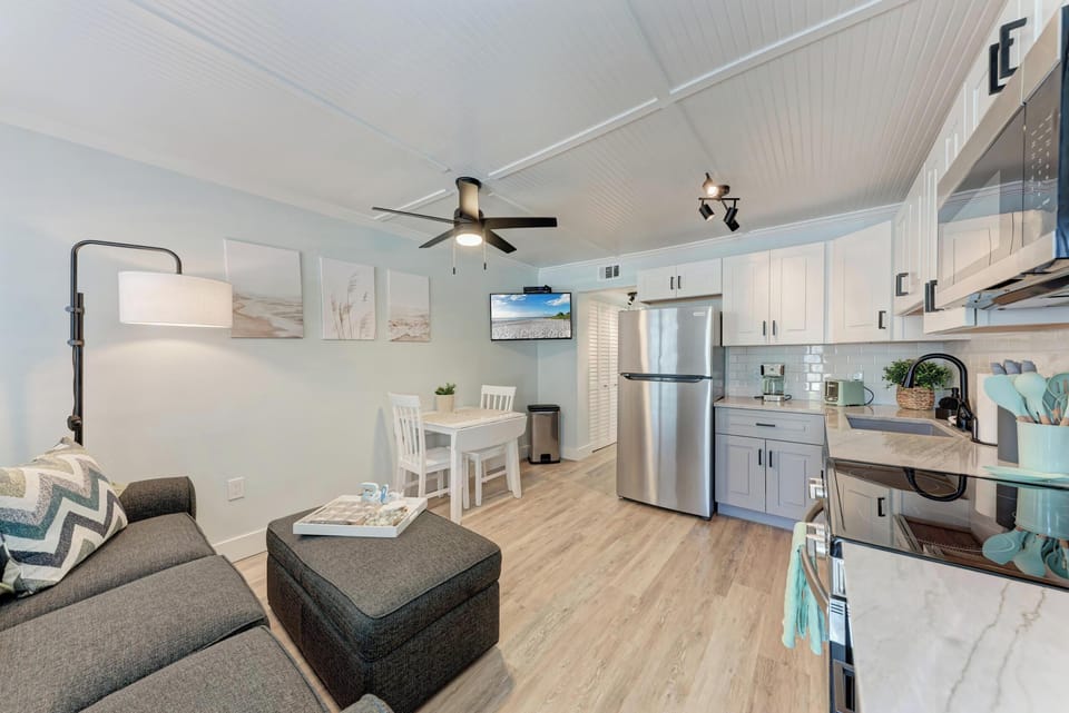 Open-concept living space with sofa, ottoman, flat screen TV, and fully equipped kitchen with stainless appliances