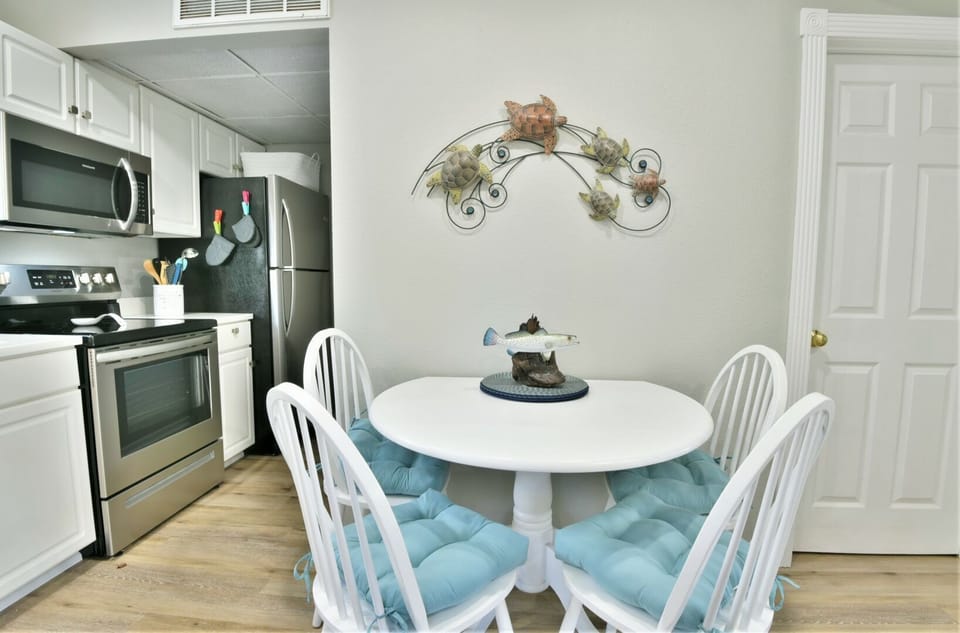 Kitchen and dining area with round table, chairs, stainless steel appliances, and teal accents