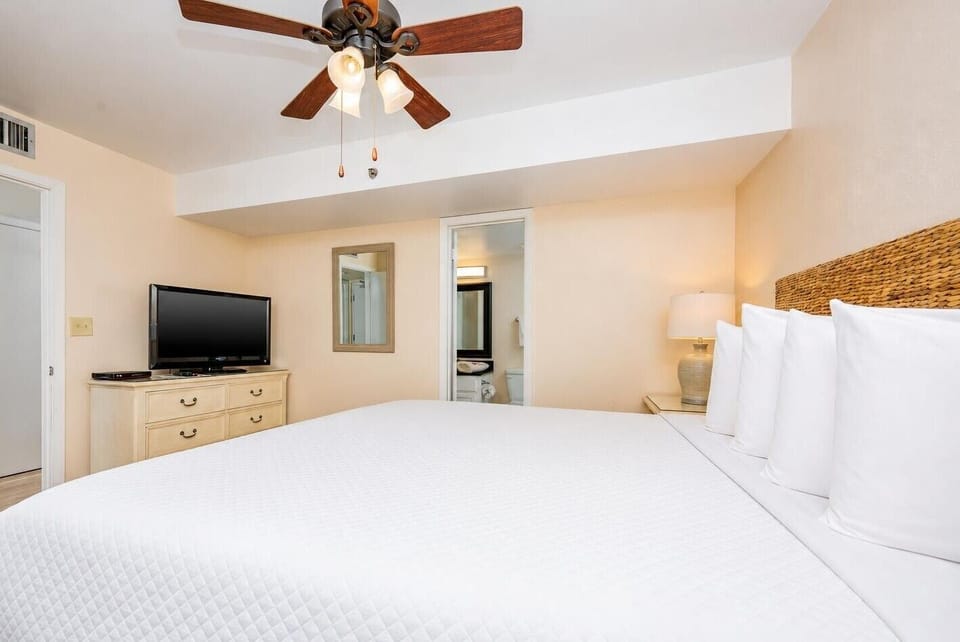 This cozy bedroom features a large king bed, a flat-screen TV, and a stylish ceiling fan, perfect for a restful getaway