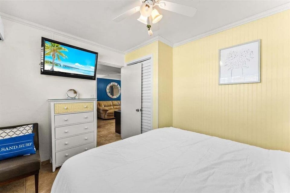 Cozy bedroom with a queen bed, smart TV, ceiling fan, and dresser — a relaxing retreat with cheerful coastal touches.