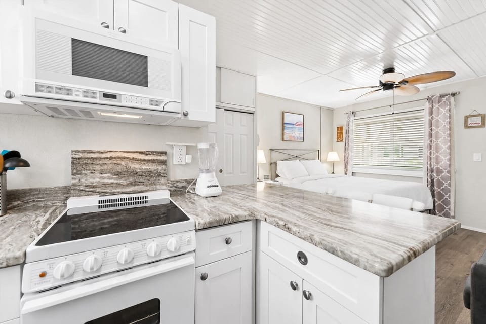 Fully equipped kitchenette with granite counters, white appliances, microwave, electric range, and bar seating for two — everything you need for a home-cooked meal.