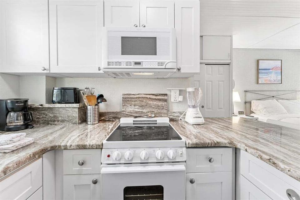 Fully equipped kitchenette with granite counters, white appliances, microwave, electric range, and bar seating for two — everything you need for a home-cooked meal.