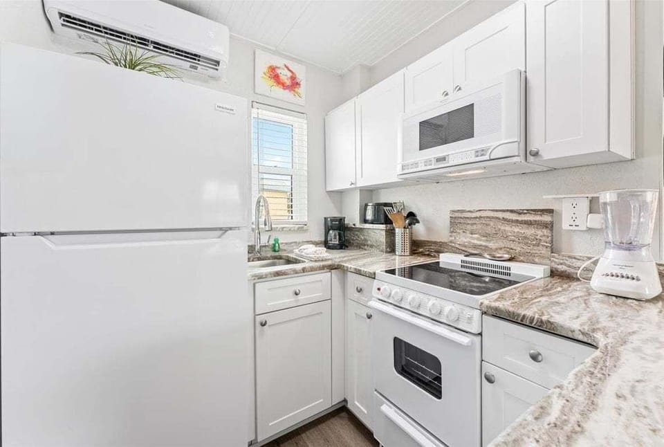 Fully equipped kitchenette with granite counters, white appliances, microwave, electric range, and bar seating for two — everything you need for a home-cooked meal.
