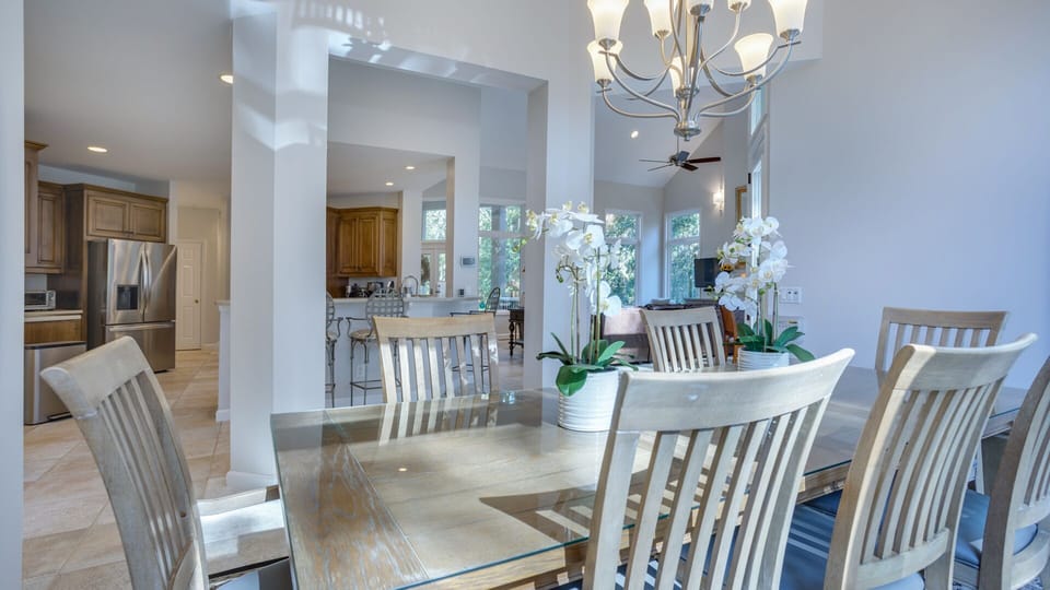 A large glass-top dining set offers plenty of seating for gatherings, while the elegant chandelier adds a warm, inviting glow.