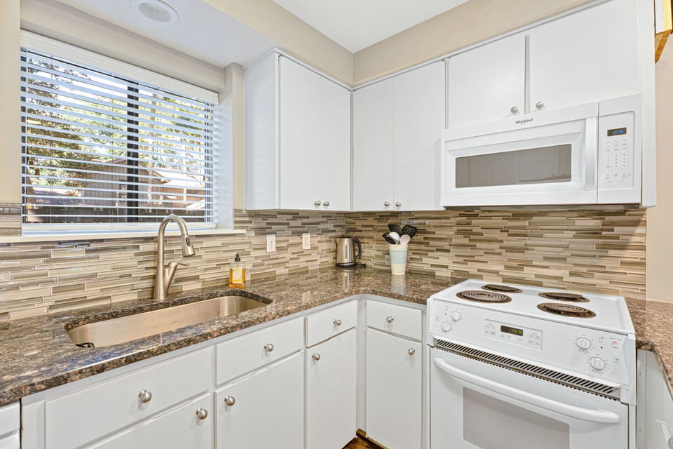 This bright, functional kitchen is designed for easy vacation living. White cabinetry keeps the space light and clean, while granite countertops and a modern tile backsplash add a polished touch.