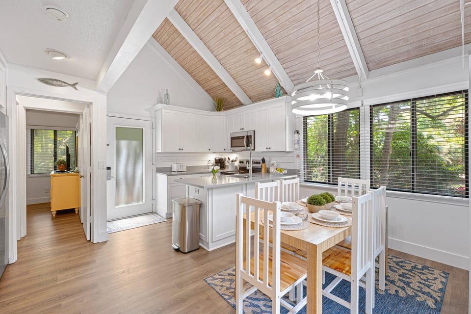 Just steps away, the adjoining dining area sits beneath a vaulted wood-plank ceiling and is surrounded by windows that fill the space with natural light.