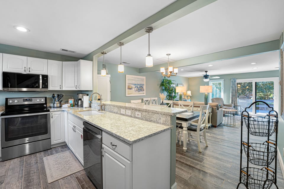A light-filled coastal kitchen featuring granite countertops, stainless-steel appliances, and open sightlines to the dining and living areas