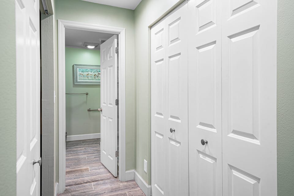 Bright hallway leading to the primary bath, featuring double closets and soft coastal tones for a serene