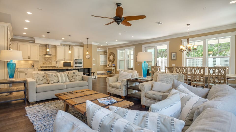 Natural light pours through large windows, highlighting the soft neutral furnishings and rich wood floors.