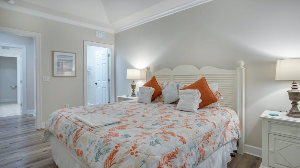 Soft color walls, wood-look flooring, and a large window overlooking the trees create a calm, beach-inspired retreat with plenty of natural light.