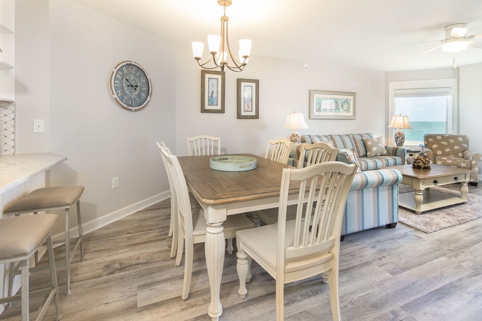 Bright coastal dining and living area with seating for six and open sightlines to the ocean. A welcoming space for shared meals, conversation, and relaxing together after a full day on the beach.