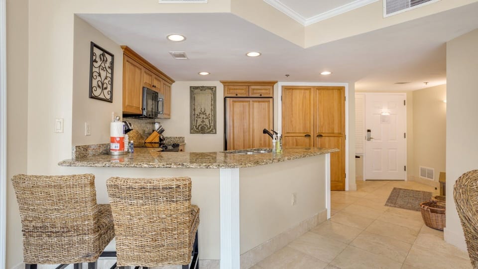 Granite countertops offer generous prep space, complemented by warm wood cabinetry and extra seating create a natural gathering spot.