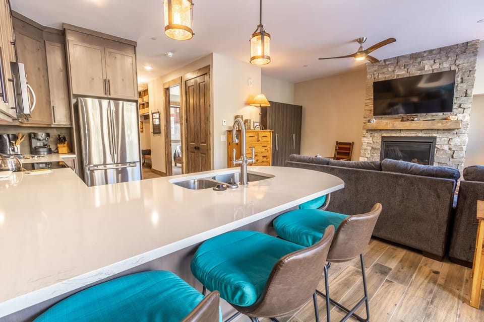 Your open-concept haven features a stunning kitchen island with turquoise accents, stone fireplace, and seamless flow to cozy living spaces.