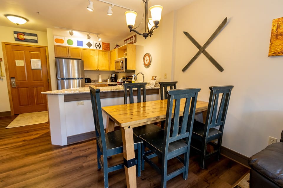 Gather around your rustic dining table where warm wood meets charming blue chairs, perfect for sharing meals in this inviting open-concept space.