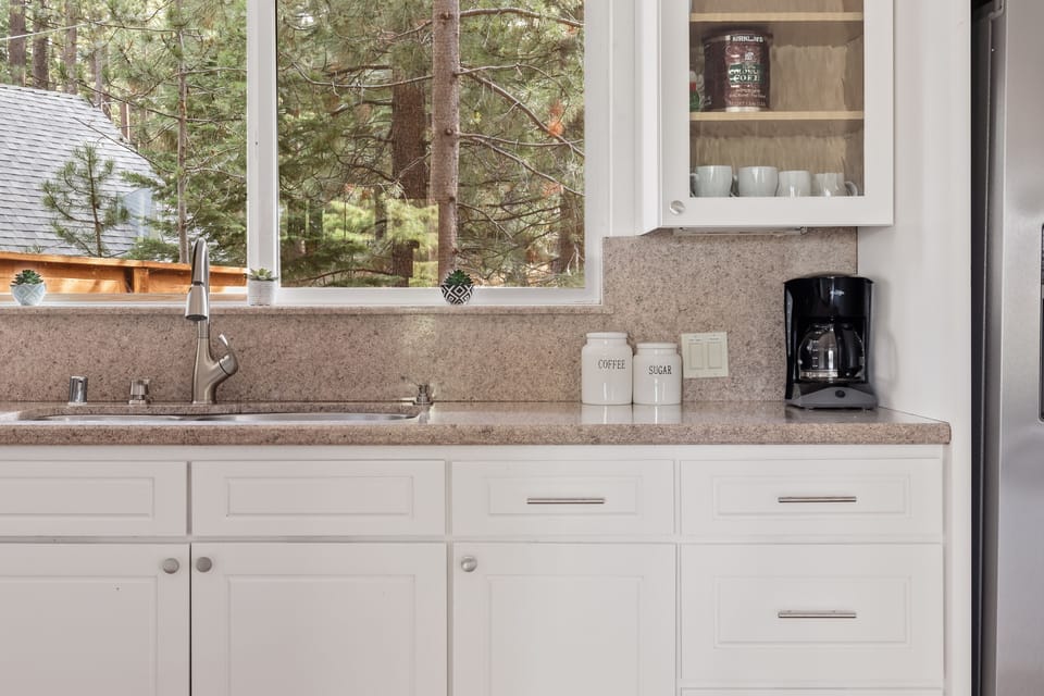 - Coffee station with drip maker and mugs ready  
- Kitchen window opens to peaceful pine views  
- Morning coffee made easy during your stay