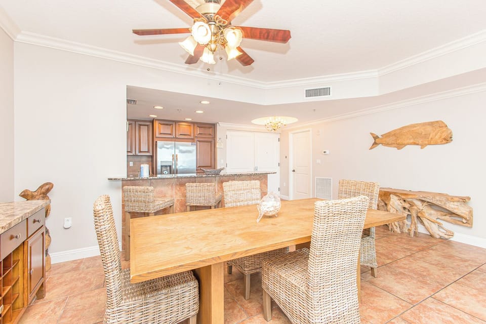 Gather around this spacious dining table where coastal charm meets comfort, with natural wood tones and wicker seating setting the tone for your beachside meals.