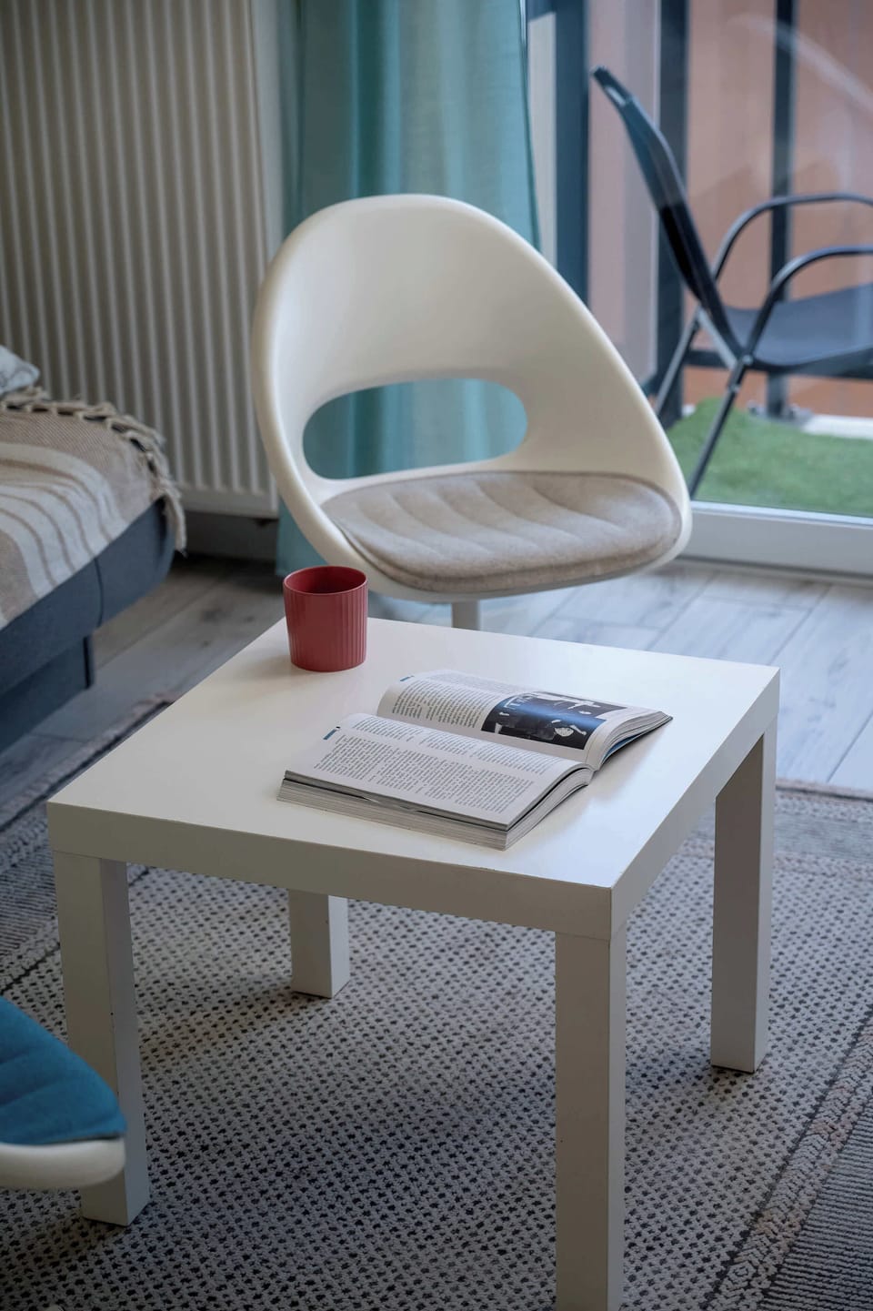 A vertical shot captures the stylish contrast between the white coffee table and a designer chair near the balcony.