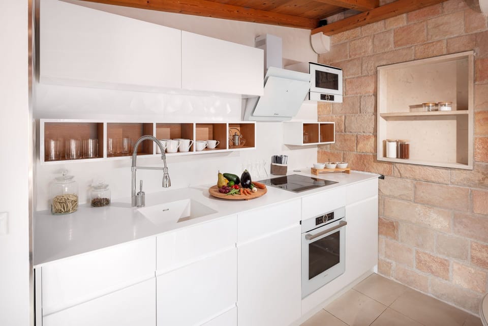 The white, modern and tall kitchen of the luxury villa Zlatni Rat in Bol on the island of Brač and the living area with a dining table with served breakfast