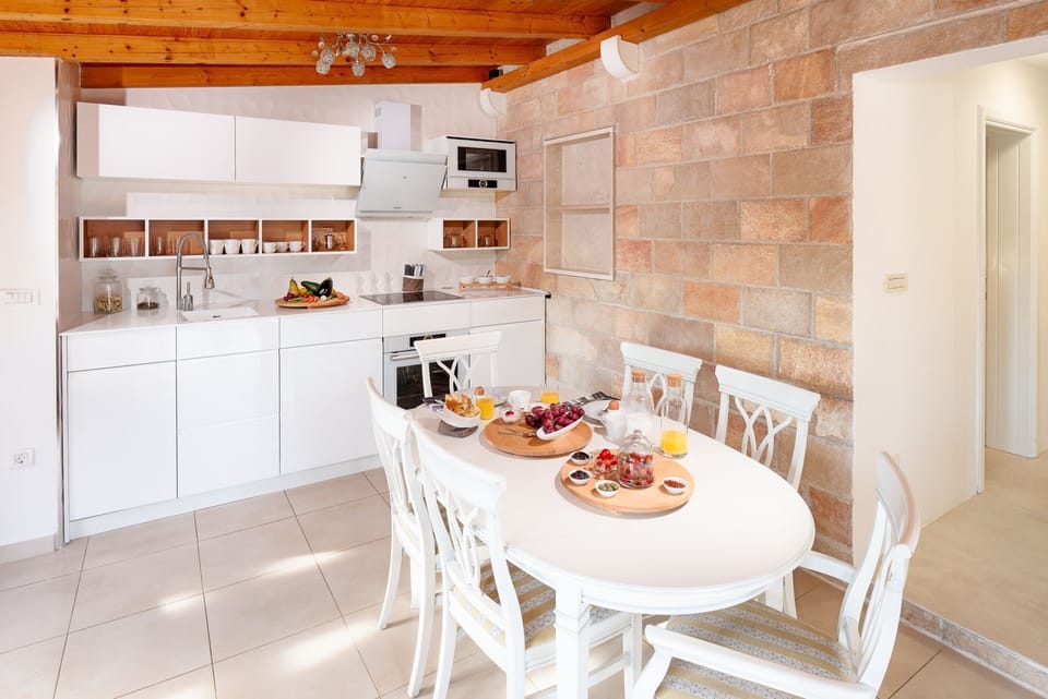 The white, modern and tall kitchen of the luxury villa Zlatni Rat in Bol on the island of Brač and the living area with a dining table with served breakfast
