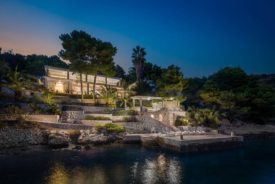 A view of Croatia luxury holiday villa on the island of Hvar, surrounded by pines and palm trees, as well as the sunbathing areas with deckchairs and the pebble beach next to the villa