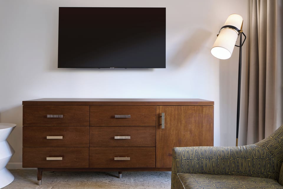Your entertainment space features a wall-mounted smart TV above elegant mid-century furniture with ample storage, soft lighting, and a cozy patterned loveseat for relaxing evenings.