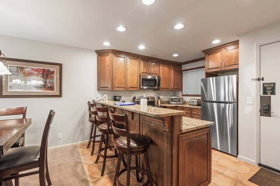 Snow Flower 135's kitchen with medium colored wood cabinets, granite counters, and 3 bar height stools at a breakfast bar.